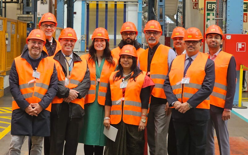 Menschen mit orangenen Warnwesten und Helmen posieren in einer Produktionshalle.