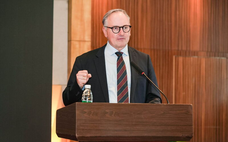 A man in a suit stands in front of a lectern.